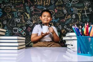 barn sitter och håller kopp i klassrummet foto