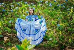 ung nikaraguanska kvinna i traditionell folk kostym i en fält av milflores, leende kvinna i nationell folk kostym i en fält omgiven förbi blommor. nikaraguanska nationell folk kostym foto