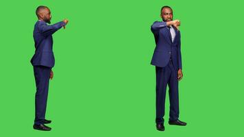 negativ kontor arbetstagare håller på med tummen ner i studio, bär formell kostym över grönskärm bakgrund. ung affärsman som visar motvilja gest och uttrycker ogillande på kamera. foto