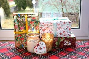 jul gåvor i lådor och brinnande ljus i glas ljusstakar nära de fönster, horisontell Foto, närbild foto