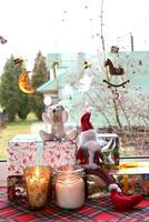 leksak gnome med teddy Björn Sammanträde på jul gåvor med ljus i glas ljusstakar nära de fönster i en lantlig hus, vertikal Foto