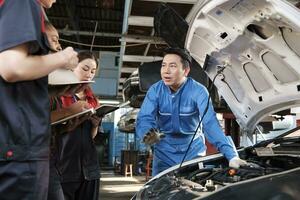 asiatisk manlig professionell bil- ingenjör handledare beskriver bil motor underhåll och reparera arbete med mekaniker arbetstagare staber team i fixera service garage, specialist yrken i bil industri. foto