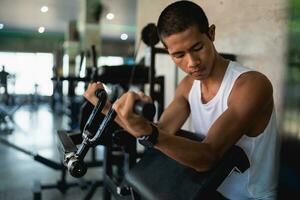 asiatisk sport man använder sig av hantel övning på Gym. asiatisk kropp byggnad för muskel Träning. sport hälsa Gym begrepp. foto