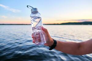 en man innehar en flaska av vatten mot de bakgrund av en sjö. foto