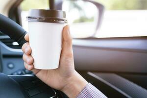 människor person företag man dricka papper kopp kaffe av varm i hand medan körning i en bil i de morgon- solljus .transport och fordon begrepp. foto