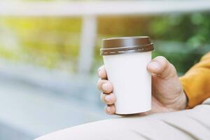 hand som håller papperskopp med take away dricker kaffe på naturligt morgonsolljus. plats för din logotyp. lämna utrymme för att skriva text. foto