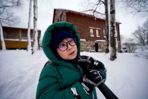 en pojke i en grön ner jacka med en skyffel står i de gård i vinter. foto