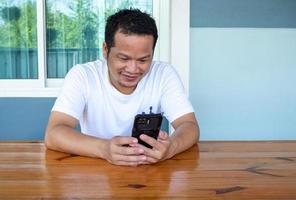 asiatisk man som bär vit skjorta med telefonen på ett träbord foto