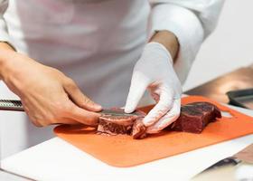 kock som skär färskt rått kött med kniv i köket