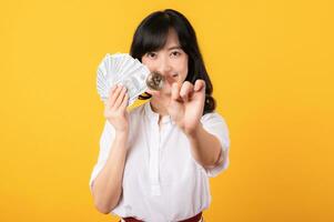 porträtt skön ung asiatisk kvinna företagspriser Lycklig leende bär vit skjorta och röd växter innehav kontanter dollar pengar och crypto digital valuta isolering på gul bakgrund. rikedom begrepp. foto