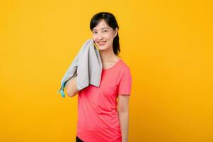 porträtt ung asiatisk sporter kondition kvinna Lycklig leende bär rosa sportkläder och ansikte handduk håller på med övning Träning träna mot gul studio bakgrund. välbefinnande och friska livsstil begrepp. foto