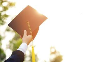 examen är fira gradering. lycka känsla hand håll visa hatt och diplom certifikat i bakgrund himmel. congratulation utbildning under början dag universitet grad. foto