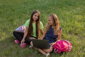 två flickor med bärbar dator sitter på gräset utanför