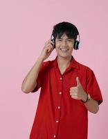 ung asiatisk le man bär hörlurar på rosa bakgrund foto