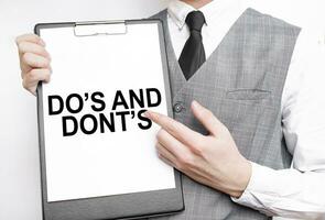 DO: s och inte inskrift på en anteckningsbok i de händer av en affärsman på en grå bakgrund, en man poäng med en finger till de text foto