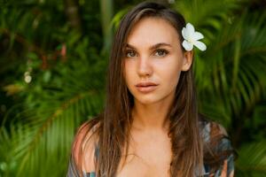 stänga graciös kvinna modell med plumeria blomma i hårstrån Framställ i tropisk natur. foto