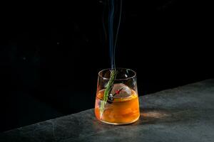 aromatisk cocktail med en kvist av tall nålar och runda is på en mörk bakgrund, sida se foto