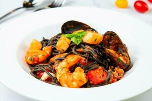 svart spaghetti med musslor, räka, tomater och örter sida se foto