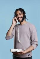 Lycklig arab man leende medan svar fast telefon telefon porträtt. glad stilig ring upp Centrum arbetstagare i tillfällig kläder talande på telefon och skrattande medan ser på kamera foto