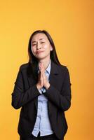 asiatisk kvinna stående med händer i bön- gest, varelse religiös i studio över gul bakgrund. andlig vuxen be Gud för förlåtelse, uttrycker tacksamhet och tro. religion begrepp foto