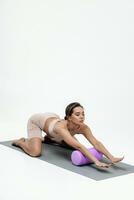 ung kvinna håller på med stretching övningar på en vit bakgrund. skum vält massage boll, kondition Utrustning för avtryckare poäng själv foto