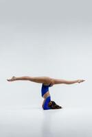 en skön smal gymnast i en träningsoverall är håller på med ben dela, stretching, yoga i en vit studio. foto