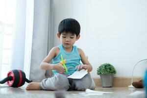 asiatisk pojke använder sig av sax till skära papper längs rader inlärning utanför de klassrum foto