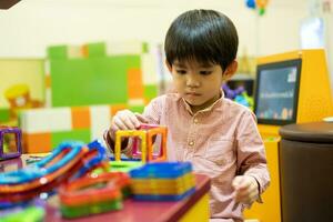 en liten asiatisk pojke är spelar med en fyrkant magnetisk pussel. foto