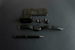 svart penna, svart smart Kolla på, smartphone, trådlös hörlurar på mörk bakgrund foto