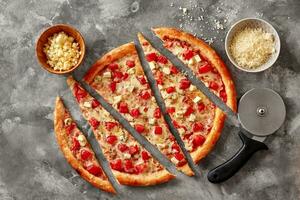 skivad pizza med tomater och blå ost på sten yta med fräs och skålar av riven mozzarella och parmesan foto