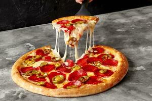 skiva av pepperoni pizza med smält mozzarella och jalapeno på tjänande spatel foto