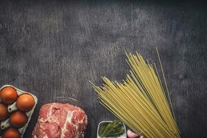 rå kött nötkött skivor på en trä- skärande styrelse med spaghetti, vitlök, kryddor, pepparkorn, salt och dill för matlagning pasta. topp se. foto