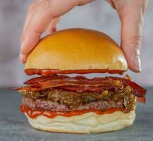 närbild av kvinnas hand innehav hamburgare med bacon. foto