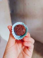hand innehav choklad tryffel i en blå papper muffin hållare foto