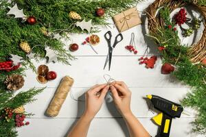 jul handgjort diy bakgrund. framställning hantverk xmas krans och ornament. topp se av vit trä- tabell med kvinna händer. foto