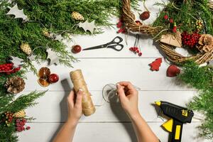 jul handgjort diy bakgrund. framställning hantverk xmas krans och ornament. topp se av vit trä- tabell med kvinna händer. foto