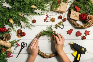 jul handgjort diy bakgrund. framställning hantverk xmas krans och ornament. topp se av vit trä- tabell med kvinna händer. foto