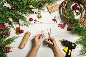 jul handgjort diy bakgrund. framställning hantverk xmas krans och ornament. topp se av vit trä- tabell med kvinna händer. foto