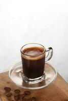svart kaffe är eras i en klar kopp med en trä- bas foto