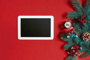 jul dekorationer och vit läsplatta med svart skärm på varm röd bakgrund. jul och ny år tema. plats för din text, lyckönskningar, logotyp. falsk upp. foto