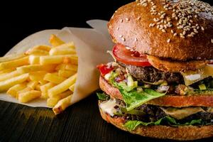 ost burger med grillad kött, ost, tomat och potatisar på mörk trä- yta. idealisk för annons. närbild foto
