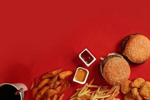 snabb mat maträtt topp se. kött hamburgare, potatis pommes frites och glas av dryck på röd bakgrund. hämtmat sammansättning. foto