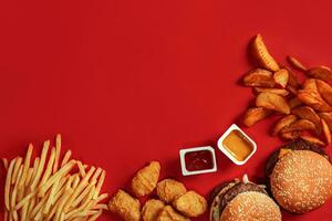 snabb mat maträtt topp se. kött hamburgare, potatis pommes frites och nuggets på röd bakgrund. hämtmat sammansättning. foto
