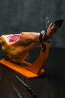 hela medelhavs traditionell jamon på en trä- stå med en kniv mager på en tabell. mörk bild foto