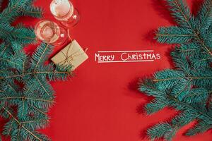 två glasögon av champagne med jul träd gren och små gåva på en röd bakgrund foto