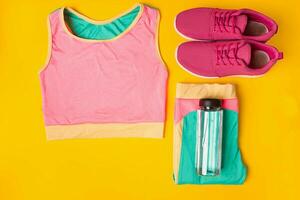 sport Utrustning. gymnastikskor och flaska av vatten på gul bakgrund foto