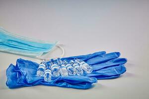 sju attrapp ampuller med transparent flytande på blå disponibel handskar och medicinsk mask isolerat på vit. coronavirus. pandemi covid19. stänga upp foto