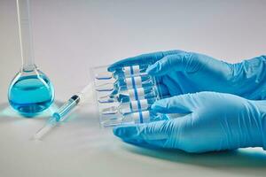 händer i disponibel handskar innehav uppsättning av ampuller med flytande. medicinsk flaska med blå kemisk reagens och spruta isolerat på vit. coronavirus foto