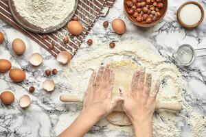 närbild skott. topp se av en bagare laga mat plats, händer är arbetssätt med en rå deg på de marmor tabell bakgrund. foto
