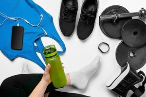 platt lägga Gym Utrustning sådan som hantlar, flaska av vattnen, smartphone med hörlurar, kondition armband och mänsklig ben i strumpor på vit bakgrund. foto